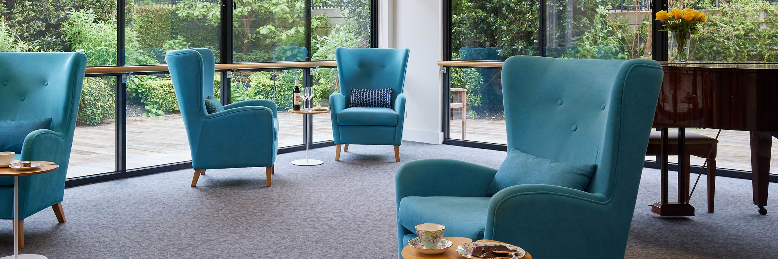 Shared sitting room detail with large comfortable bright blue armchairs and large windows in background.